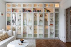 a living room filled with white furniture and lots of bookshelves on the wall