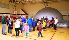 a group of people standing in front of an airplane on a gym floor with red lines