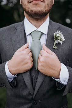 a man in a suit adjusts his tie and flower boutonniere on his lapel