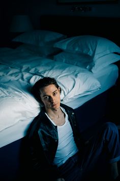 a man sitting on the floor in front of an unmade bed with white sheets