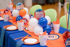 the table is set with balloons, plates and cups for an orange blue and white birthday party