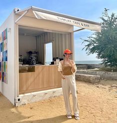 a woman standing in front of a food cart on the beach with her hand up to her face