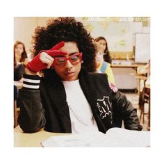 a young man sitting at a table in front of a laptop computer wearing red glasses