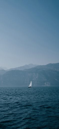 a sailboat sailing on the ocean with mountains in the background