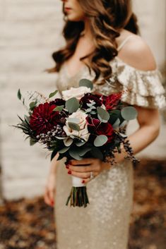 a woman holding a bouquet of red and white flowers in front of a brick wall