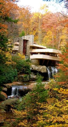 a house in the woods surrounded by trees with fall foliage and water running through it