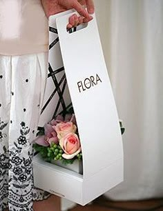 a person holding a box with flowers in it that says flora on the front and side