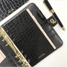 a black and gold planner with a pen next to it on top of a white table