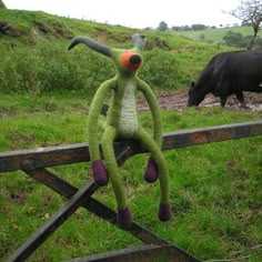 a green stuffed animal sitting on top of a wooden fence next to a black cow