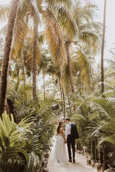 a bride and groom standing in the middle of palm trees