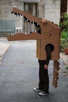 a young boy is wearing a cardboard dinosaur costume