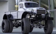 an old truck is parked in front of a building with large tires on it's flatbeds