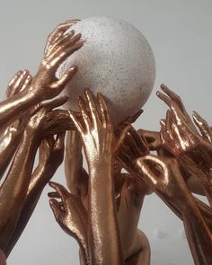 several hands reaching for a white ball in the middle of gold foiled hand prints