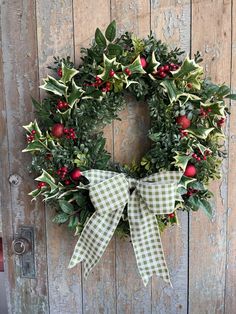 a christmas wreath hanging on the side of a wooden door with greenery and berries