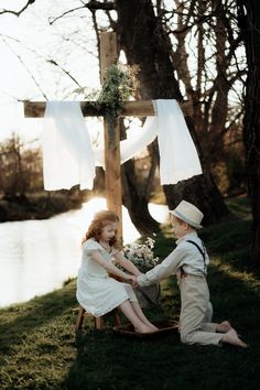 two children are sitting on the ground near a cross and holding hands with each other