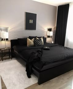 a bed with black sheets and pillows in a bedroom next to two lamps on either side of the bed