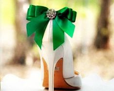 a white high heel shoe with a green bow on the top and bottom, sitting on a table in front of some trees