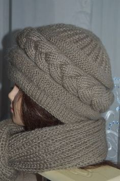 a woman wearing a knitted hat with her hands on her head and looking out the window