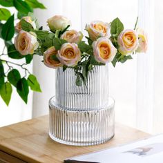 a vase filled with pink and yellow roses on top of a wooden table next to a window