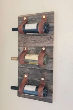 two wine bottles are hanging on the wall with leather straps, and one bottle is empty