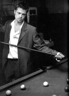 a man standing next to a pool table holding a cue in one hand and looking at the ball