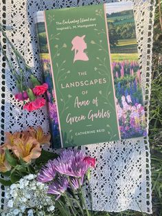 an open book sitting on top of a lace covered table cloth next to colorful flowers