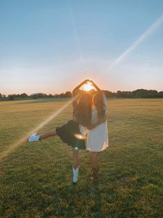 two people are standing in the grass with their arms around each other as the sun sets