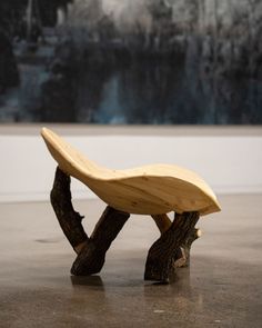 a wooden bench sitting on top of a cement floor next to a tree branch sculpture