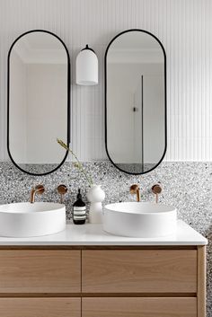 two round mirrors are above the double sinks in this modern bathroom with white walls and flooring