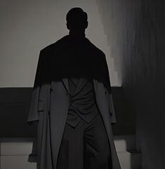 a man standing in the dark with his back to the camera, wearing a cape