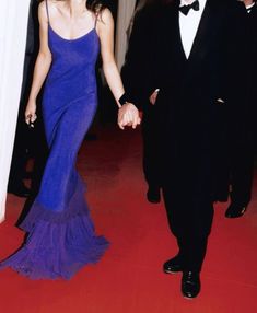 a man and woman in formal wear walking down a red carpeted hallway holding hands