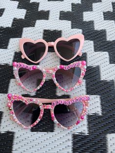 two pairs of pink sunglasses with hearts on them sitting on a black and white checkered surface