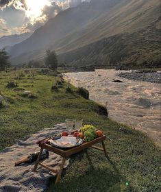 a picnic on the bank of a river with mountains in the background and sun shining through clouds