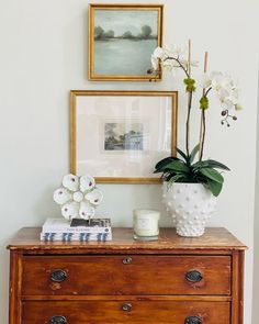 a wooden dresser with flowers and pictures on the wall