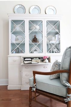 a chair sitting in front of a china cabinet with plates on the top and bottom