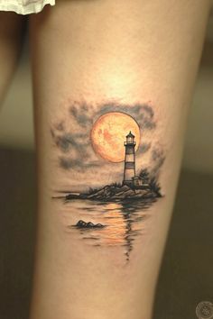 a woman's leg with a lighthouse tattoo on it and the moon in the background