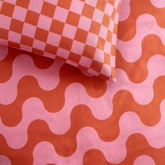 an orange and pink bed sheet with wavy design on it, next to a pillow