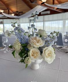 a vase filled with white and blue flowers on top of a long table covered in tables cloths