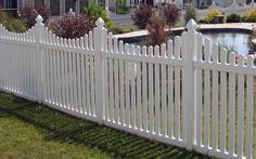 a white picket fence in front of a large house with a swimming pool and landscaping