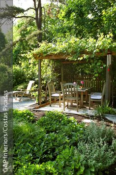 an outdoor dining area in the middle of a garden surrounded by trees and bushes with chairs around it