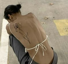 a woman sitting on the ground with her back turned to the camera, wearing a tattoo