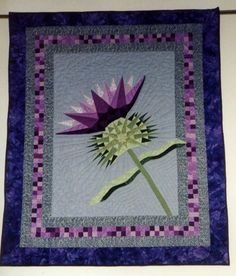 a purple and white quilted wall hanging with a flower on it's center