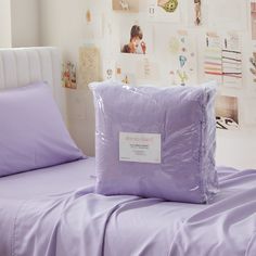 a bed with purple sheets and pillows in a room that has pictures on the wall