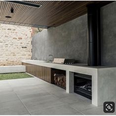 an outdoor fireplace in the middle of a patio with a stone wall and wooden ceiling