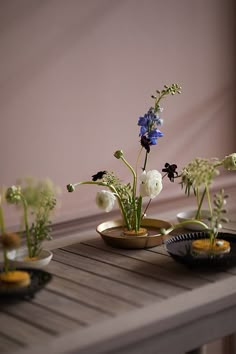 three small vases filled with flowers sitting on top of a wooden table next to each other