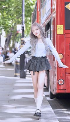 a young woman is walking down the sidewalk in front of a red double decker bus