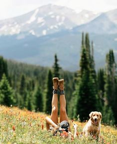 a person laying in the grass with their feet up and a dog standing behind them