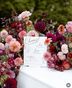 a table topped with lots of flowers next to a white sign that says cheers on it