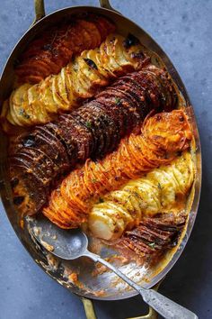 a pan filled with potatoes and meat on top of a blue countertop next to a spoon