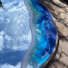 a reflection of the sky and clouds in a glass sculpture that looks like an ocean wave